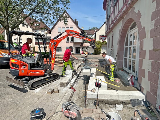 Astreine Leistung: Mitarbeiter der Gemeinde versetzen neue Treppenstufen als Stütze bzw. Begrenzung für die barrierefreie Rampe zum neuen Zugang auf der Westseite der Bücherei.