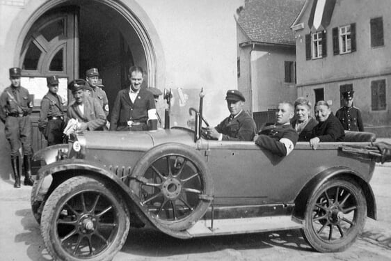 Wahltag in Nordheim. Wer nicht laufen konnte, wurde gefahren. Fahrer: Otto Frank. Stehend mit Armbinde Fritz Gerlach, sitzend mit Binde Ludwig Daab. Hinten im Auto Frau Erichsen und Frau M&uuml;ller. Rechts hinten Schutzmann L&auml;chele.