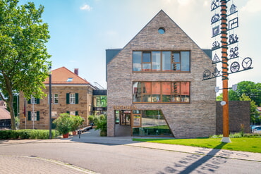 Backsteingeb&auml;ude mit spitzem Dach, daneben ein weiteres Geb&auml;ude
